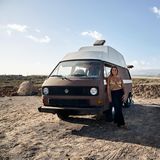 Joy steht an ihrem Van gelehnt am Strand