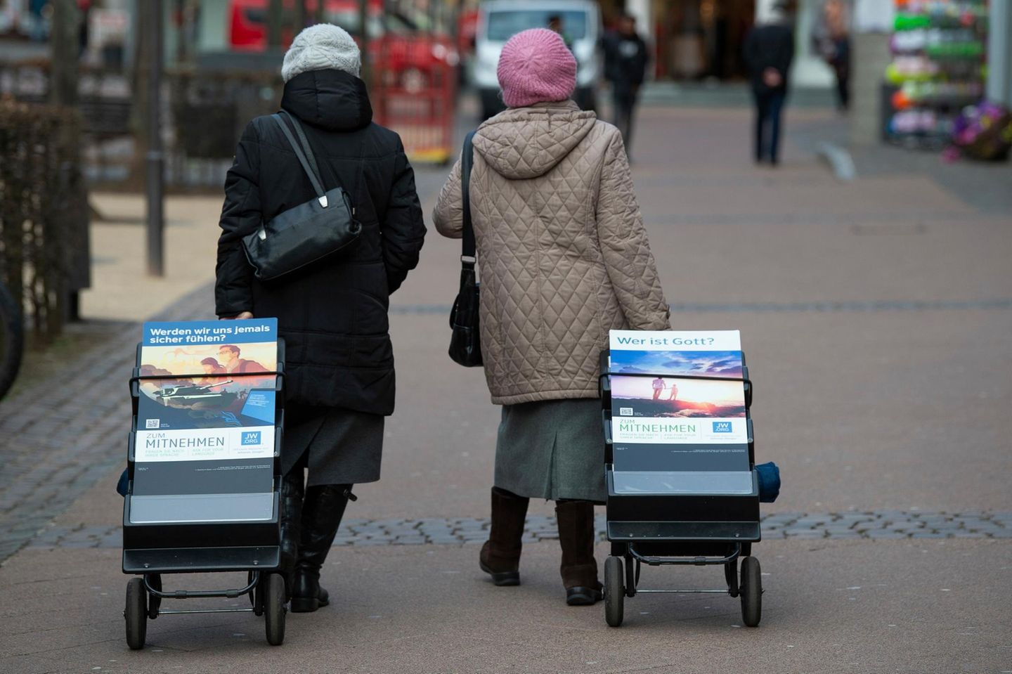 zwei ältere Damen laufen durch die Innenstadt. Im Schlepptau jeweils ein Zeitschriftenständer