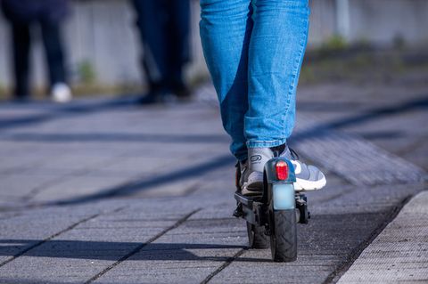 Die Beine eines Jugendlichen stehen auf einem E-Scooter