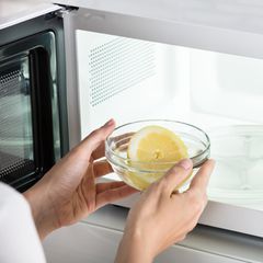 Nahaufnahme einer Frau, die eine Schüssel mit Zitronenscheiben in die Mikrowelle stellt
