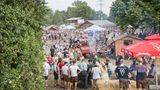 Ein ländliches Festivalgelände im Grünen. Manche Menschen tragen eine Tracht.