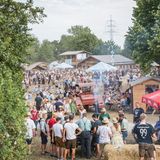 Ein ländliches Festivalgelände im Grünen. Manche Menschen tragen eine Tracht.
