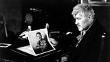 Mario Adorf hält ein Foto von Hitler in den Händen und schaut zur Seite