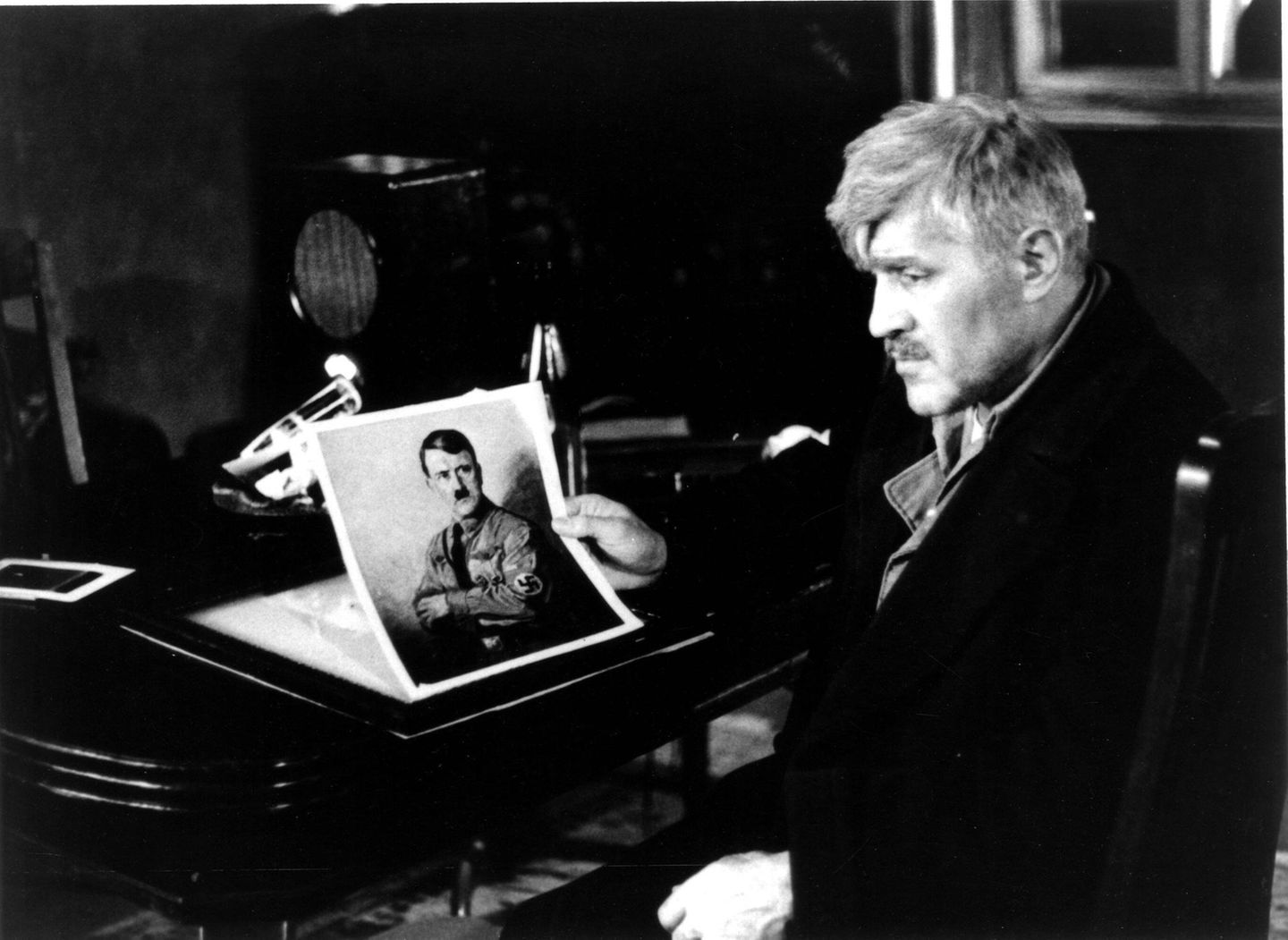 Mario Adorf hält ein Foto von Hitler in den Händen und schaut zur Seite