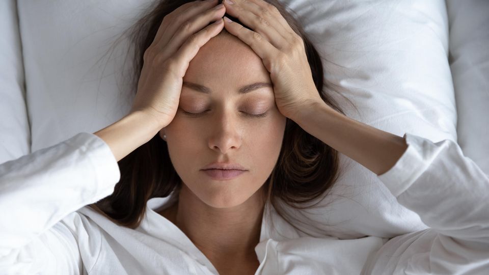 Schlafprobleme: Eine Frau liegt im Bett und fasst sich an den Kopf