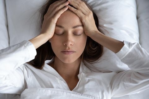 Schlafprobleme: Eine Frau liegt im Bett und fasst sich an den Kopf