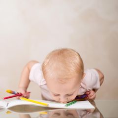 Ein Kleinkind mit Buntstiften innder Hand beißt in ein Buch