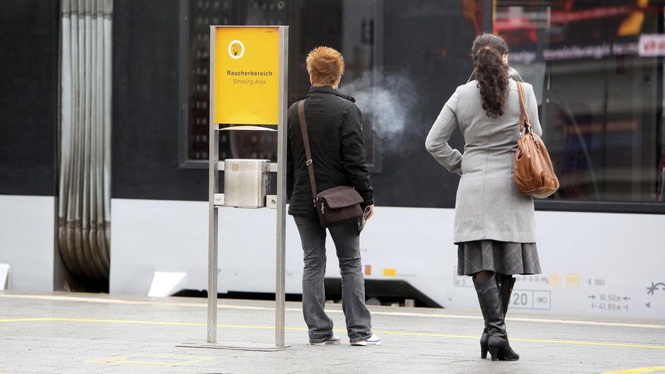 Zwei Rauchende stehen an einer Haltestelle der Deutschen Bahn in Bochum