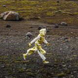 Ein Mensch in goldenem Outfit läuft durch eine karge Landschaft