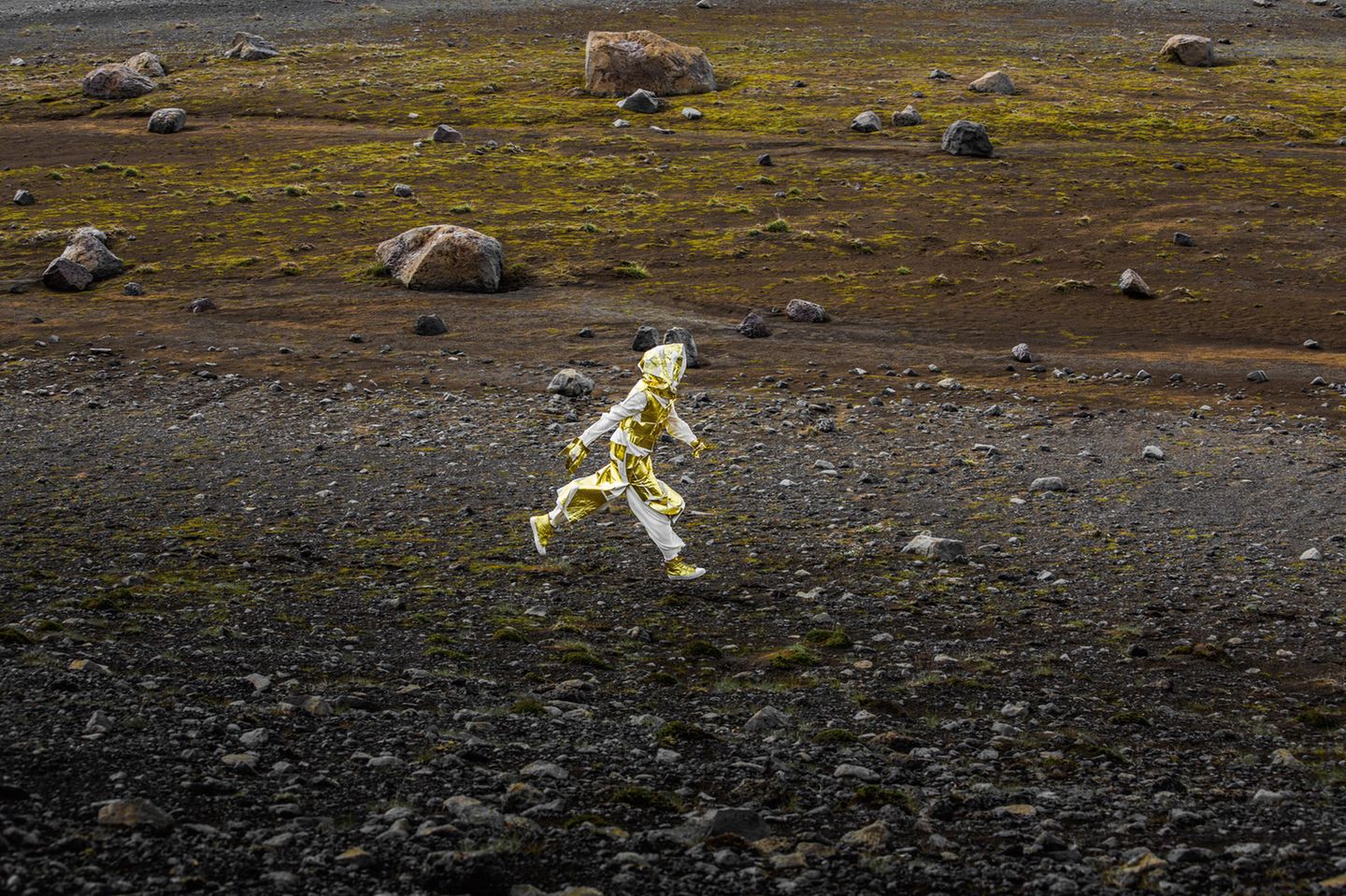 Ein Mensch in goldenem Outfit läuft durch eine karge Landschaft