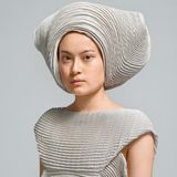 Eine junge Frau mit einem grauen Ensemble aus einem Hosenkleid und einem ausladenden Hut