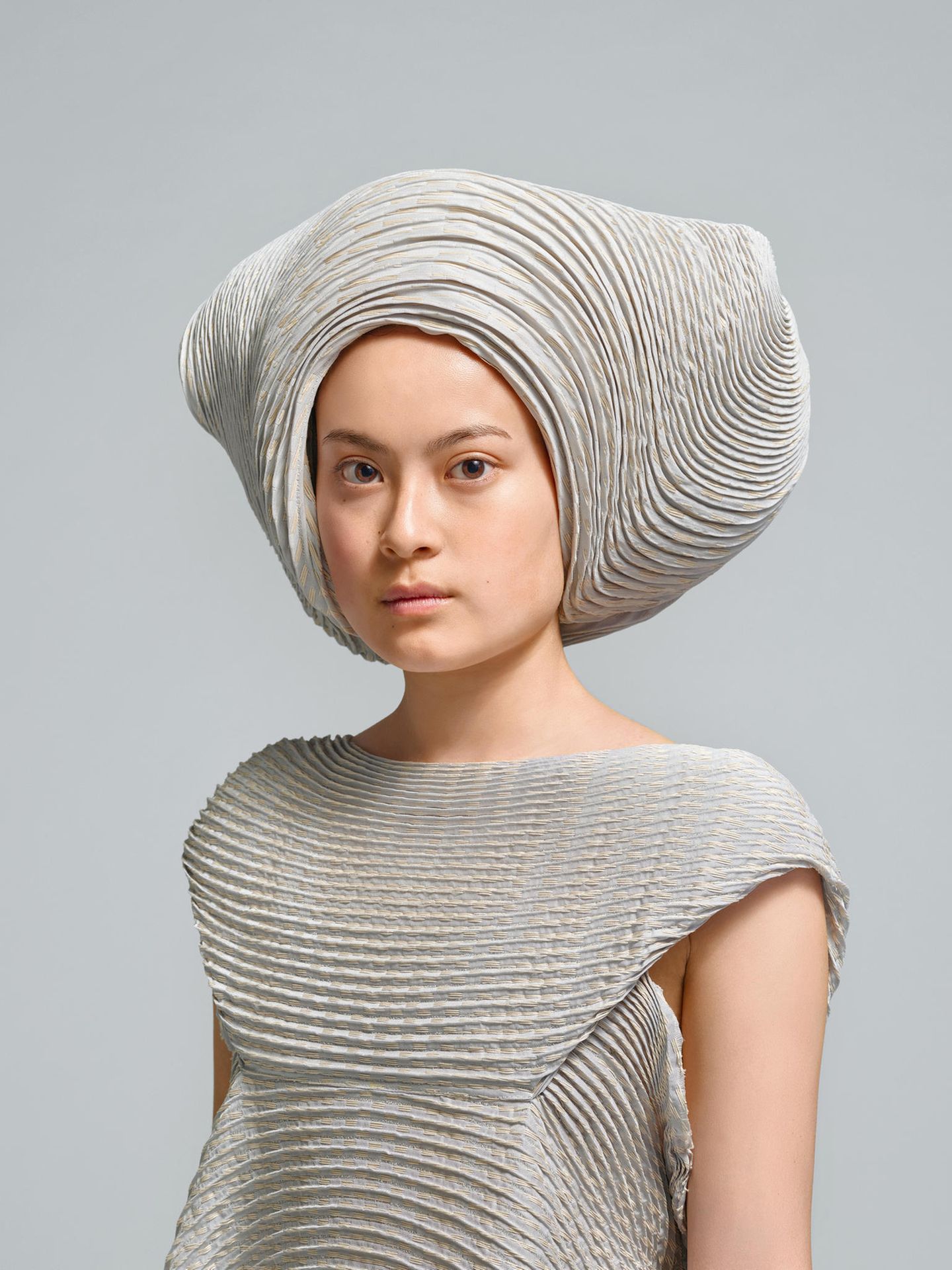 Eine junge Frau mit einem grauen Ensemble aus einem Hosenkleid und einem ausladenden Hut