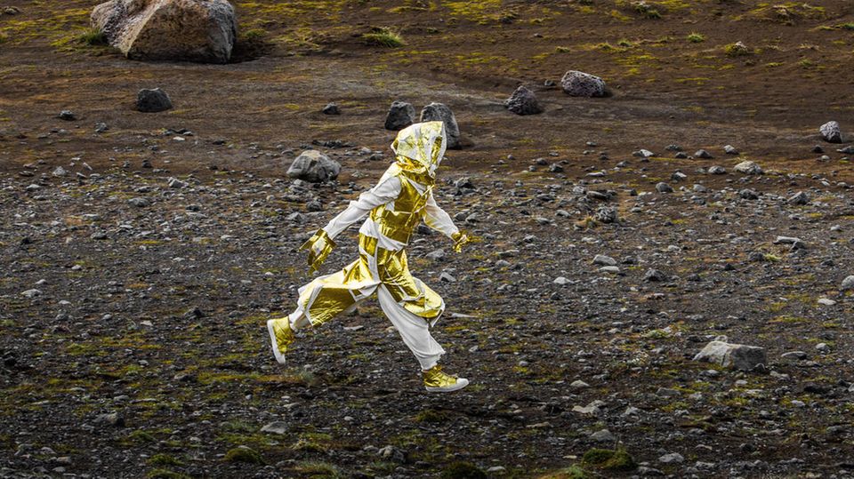 Ein Mensch in goldenem Outfit läuft durch eine karge Landschaft