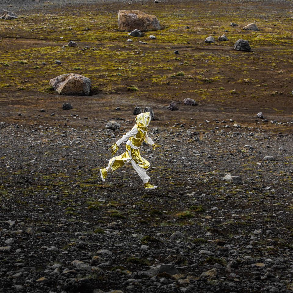 Ein Mensch in goldenem Outfit läuft durch eine karge Landschaft