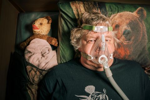 Torsten Herrmann (Doc Mabuse) in seinem Bett in der Reha-Einrichtung mit Atemmaske, daneben ein Teddybär