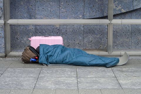 Ein mutmaßlich von Wohnungslosigkeit Betroffener liegt in einem Schlafsack auf dem Bürgersteig