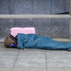 Ein mutmaßlich von Wohnungslosigkeit Betroffener liegt in einem Schlafsack auf dem Bürgersteig