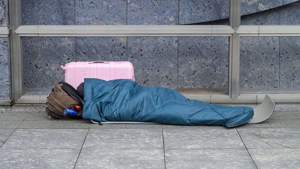 Ein mutmaßlich von Wohnungslosigkeit Betroffener liegt in einem Schlafsack auf dem Bürgersteig