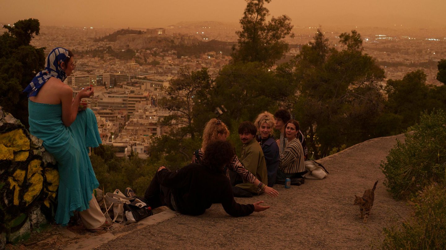 Touristen spielen mit einer Katze auf dem Lycabettus-Hügel, während im Hintergrund eine unheimliche Atmosphäre in Athen herrscht. Die Region Attika rund um Athen sei aufgrund klimatischer Bedingungen regelmäßig vor allem im Frühjahr und Herbst von dem Phänomen betroffen, sagten Meteorologen der Tageszeitung "Kathimerini".
