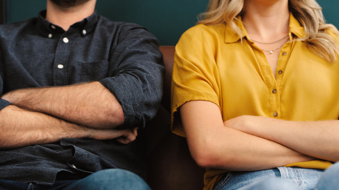 Beziehungsprobleme: Ein Paar sitzt nebeneinander auf dem Sofa mit verschränkten Armen