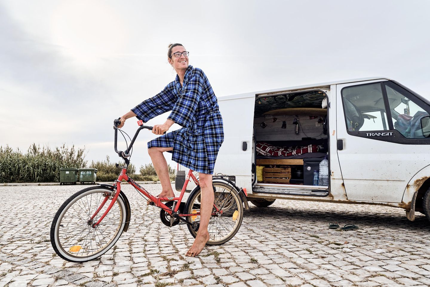 Limo sitzt auf seinen Fahrrad auf einem Parkpltz. Im Hintergrund steht sein Camper Limo sitzt auf seinen Fahrrad auf einem Parkpltz. Im Hintergrund steht sein Camper