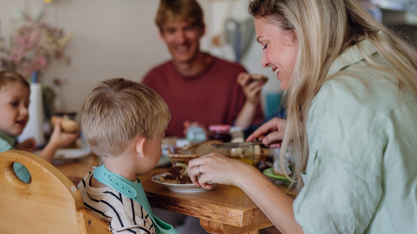 Familie sitzt beim Essen und Mutter schneidet ihrem Sohn das Brot