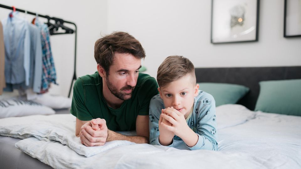 Ein Vater spricht mit seinem Sohn auf dem Bett.
