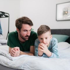 Ein Vater spricht mit seinem Sohn auf dem Bett.
