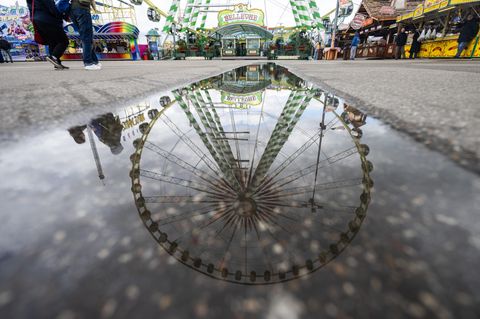 Ein Riesenrad spiegelt sich in einer Pfütze auf dem Festgelände des Stuttgarter Frühlingsfestes