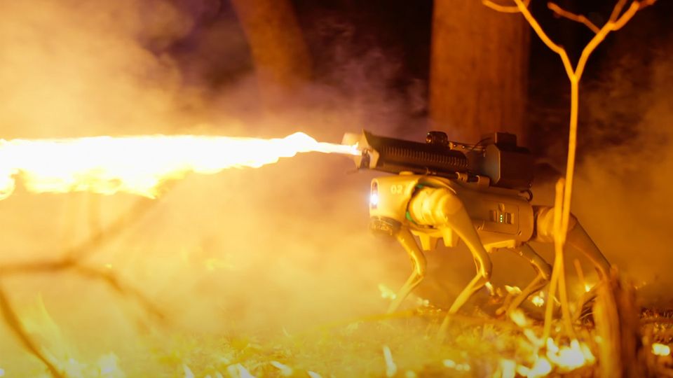 Ein Roboter mit Flammenwerfer auf dem Rücken steht im Wald.