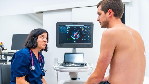 Rückansicht eines männlichen Patienten und einer Ärztin, die Ergebnisse eines Echokardiogramms betrachten