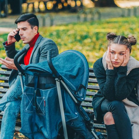 Paar mit Kinderwagen im Park, Frau guckt gedankenverloren