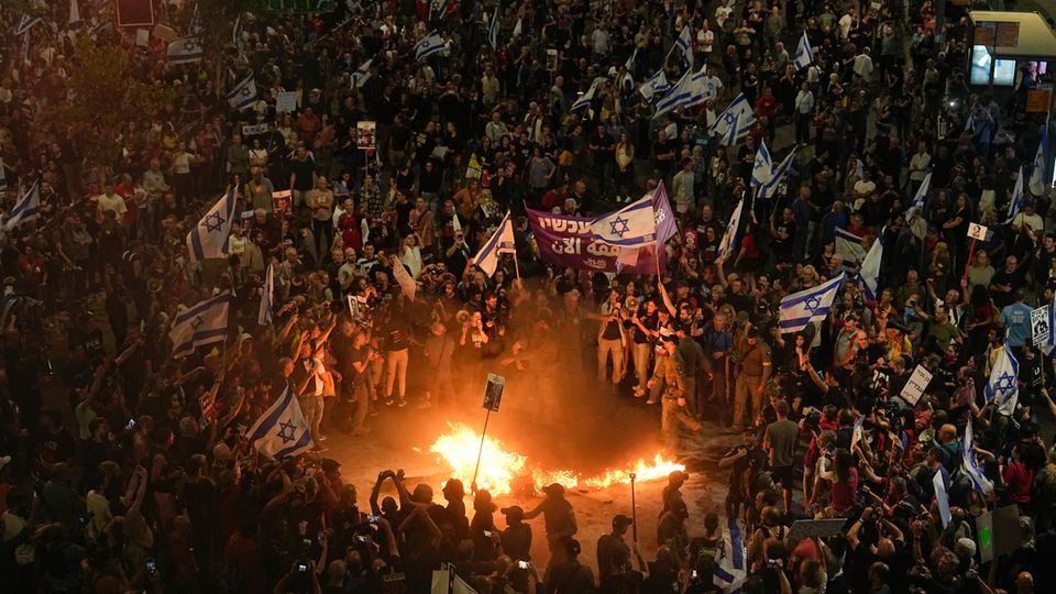 Eine Menschenmenge mit Flaggen Israels steht um ein Feuer herum und fordert Geisel-Freilassungen