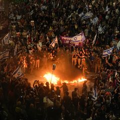 Eine Menschenmenge mit Flaggen Israels steht um ein Feuer herum und fordert Geisel-Freilassungen