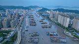 An einem Hafen in China liegen Boote, Seite an Seite, im Hintergrund sieht man eine Stadt.