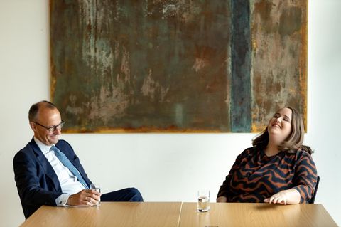 Friedrich Merz und Ricarda Lang sitzen an einem Tisch und lachen