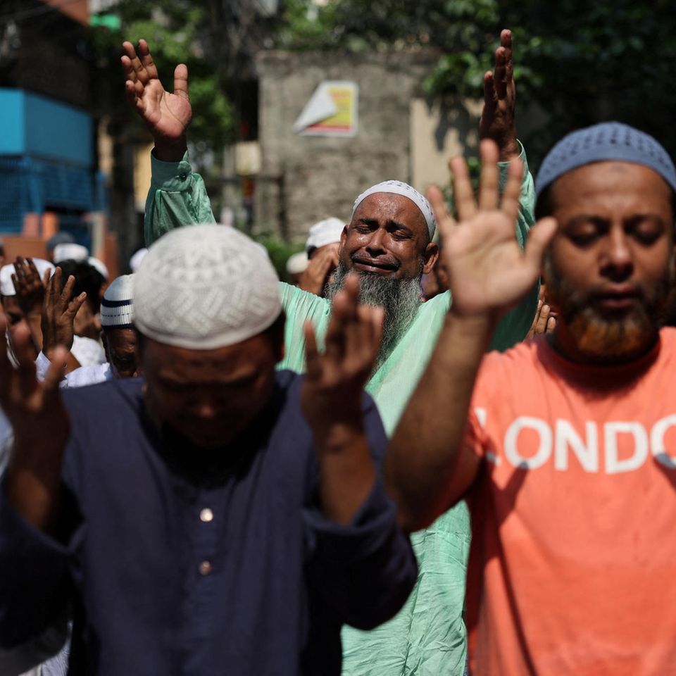 Eine Gruppe Menschen in T-Shirts in Bangladesch wendet die Hände gen Himmel, die Augen geschlossen.