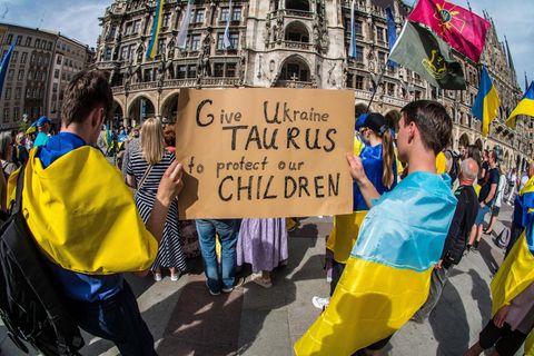Menschen in München haben Ukraine-Fahnen umgebunden und halten ein Plakat, das die Lieferung fordert.