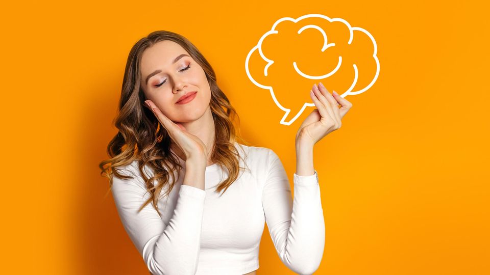 Junge Frau vor orangefarbenem Hintergrund hält ein gezeichnetes Gehirn hoch und schließt die Augen