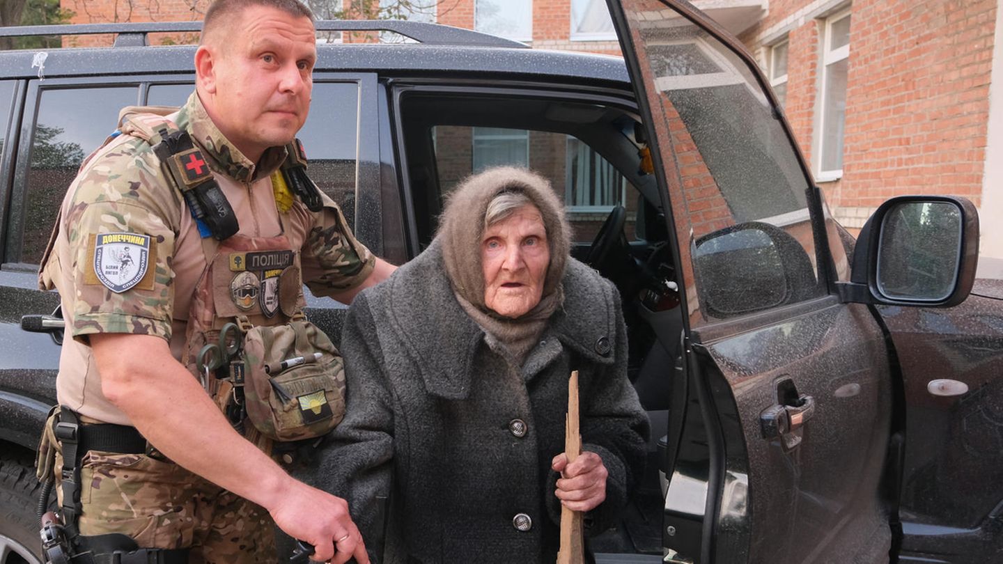 Ein Brett als Gehstock nutzen: Ein ukrainischer Polizist hilft der 97-jährigen Lidia Lomikovska