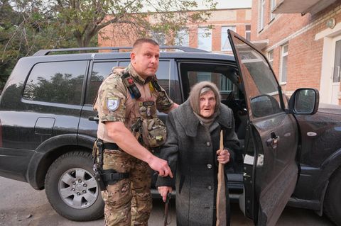 Mit einem Brett als Gehstock: Ein ukrainischer Polizist hilft der 97-jährigen Lidia Lomikovska
