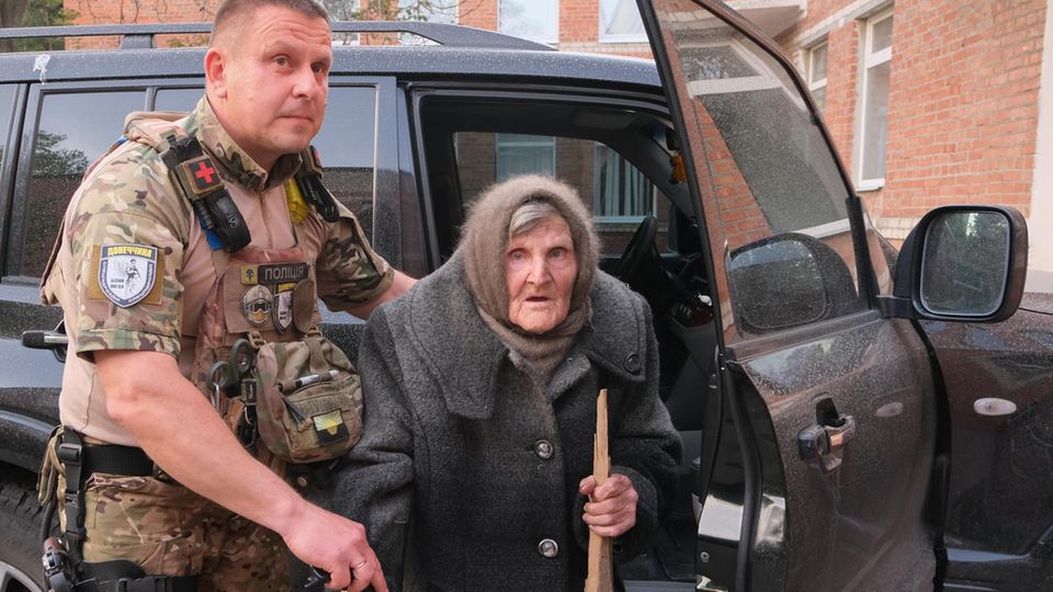 Mit einem Brett als Gehstock: Ein ukrainischer Polizist hilft der 97-jährigen Lidia Lomikovska