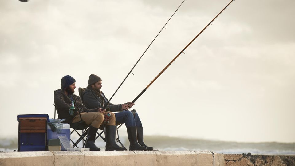 Geschenke für Angler: Zwei Männer sitzen auf einem Steg und angeln zusammen