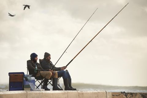 Geschenke für Angler: Zwei Männer sitzen auf einem Steg und angeln zusammen