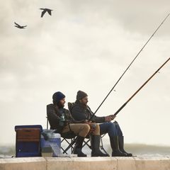 Geschenke für Angler: Zwei Männer sitzen auf einem Steg und angeln zusammen