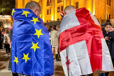In Georgien ist ein Demonstrant in eine EU-, der andere in eine georgische Flagge gehüllt