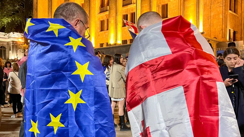 In Georgien ist ein Demonstrant in eine EU-, der andere in eine georgische Flagge gehüllt