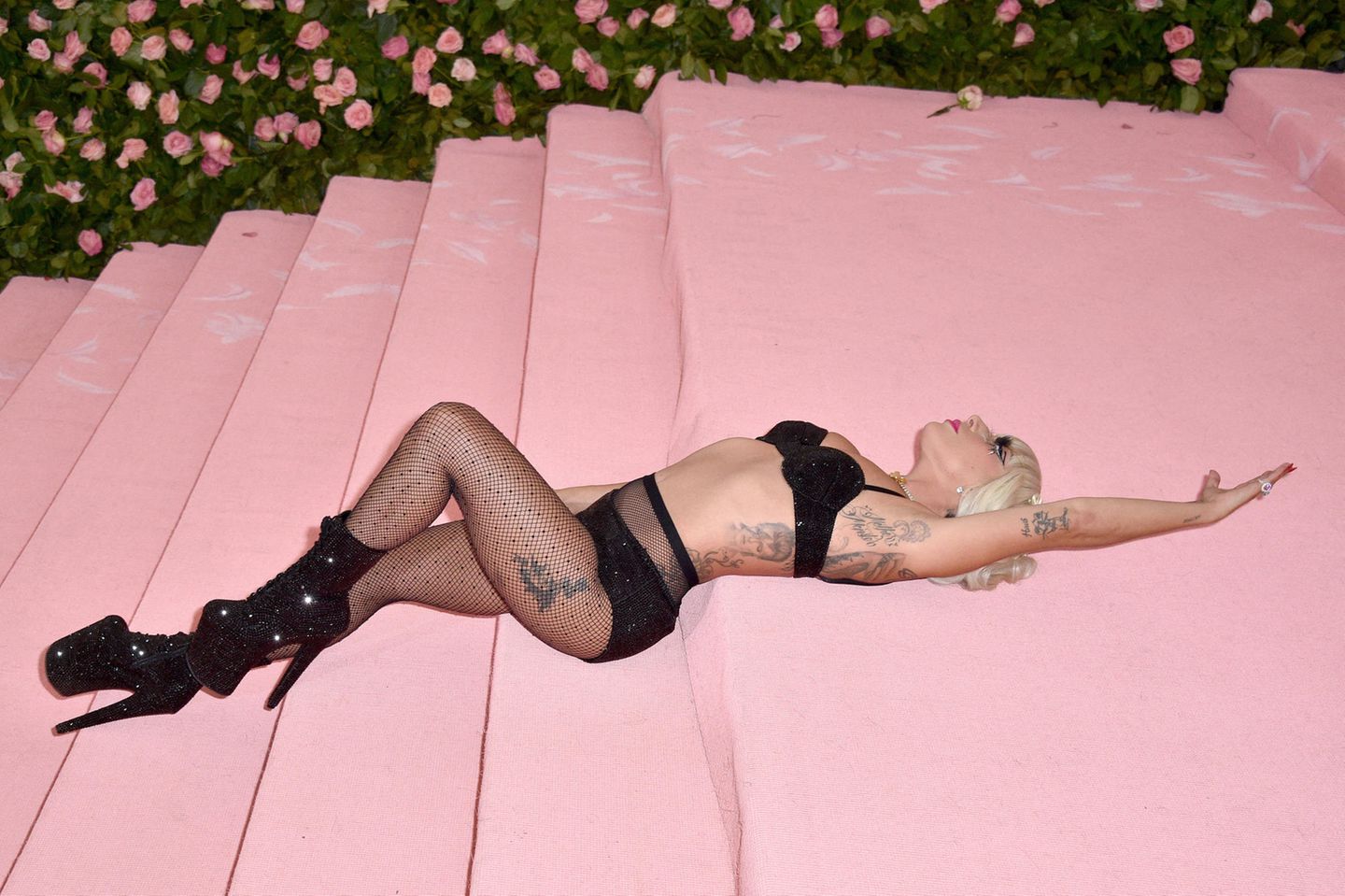 Lady Gaga räkelt sich im schwarzen Lingerielook auf dem rosafarbenen Teppich der Met Gala 2019
