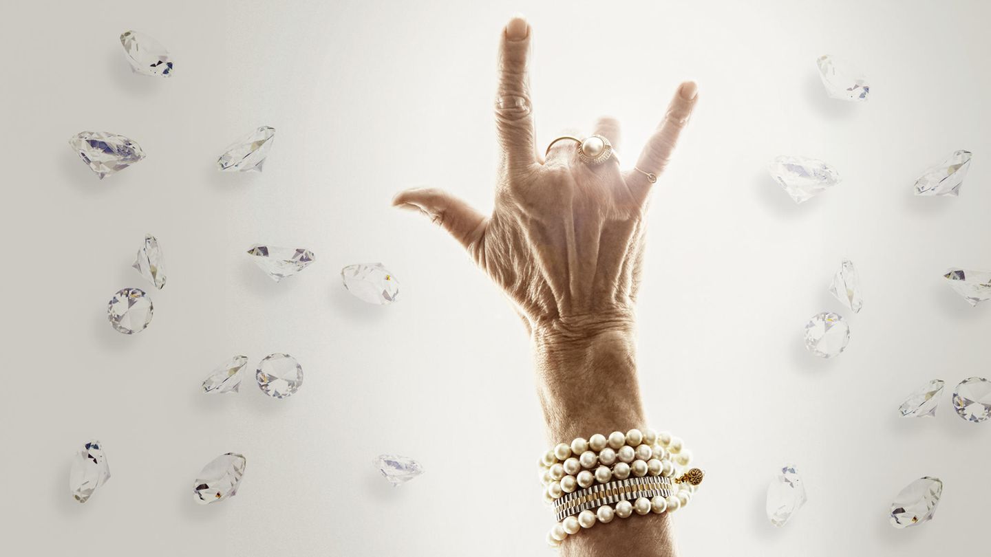 Eine faltige Hand einer Frau mit viel Schmuck zeigt eine Corna ( gehörnte Hand)