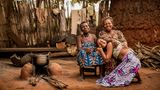 Drei Frauen (Großmutter, Mutter und Tochter) sitzen eng beieinander in Benin auf der Erde
